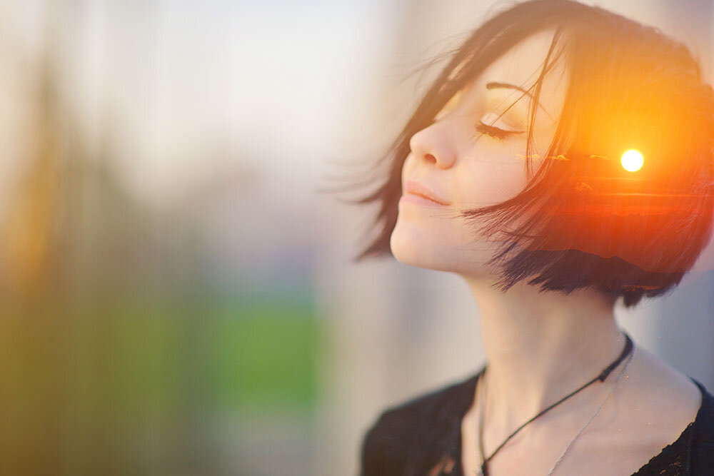 A woman with her eyes closed, face turned toward the light